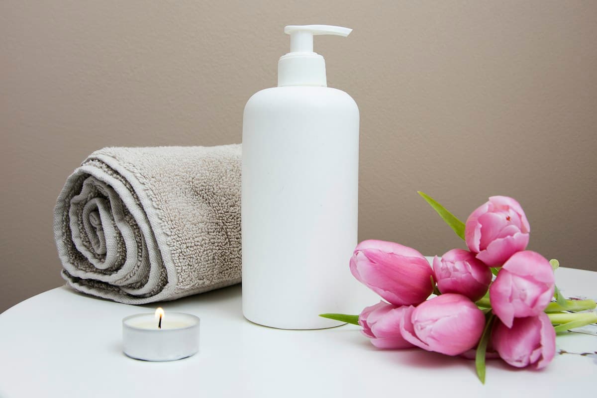 White body care bottle, folded towel, candle and pink flowers